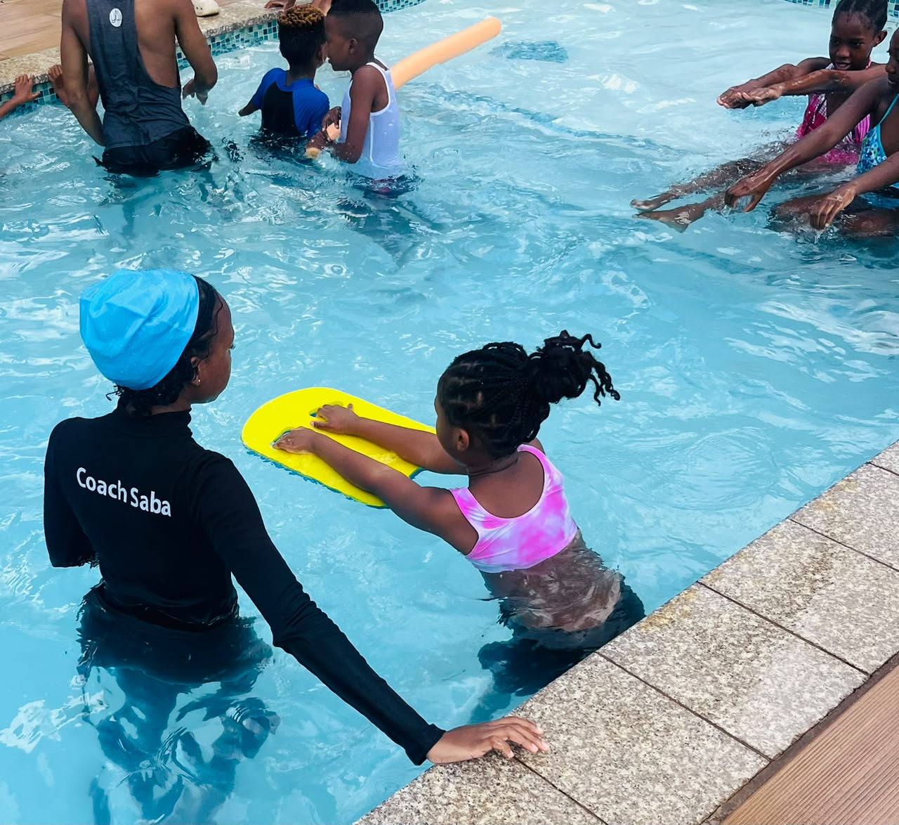 AquaMasters coach helping a child practise kicking with a kickboard in the pool
